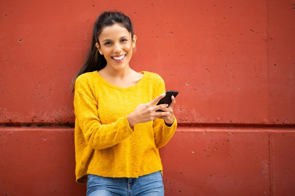 Retrato Sonriente Mujer Joven Sosteniendo Teléfono Celular Por Pared Roja —  Fotos de Stock
