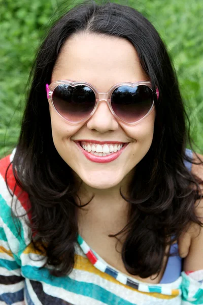 Beautiful young girl in sunglasses sitting on the grass — Stock Photo, Image