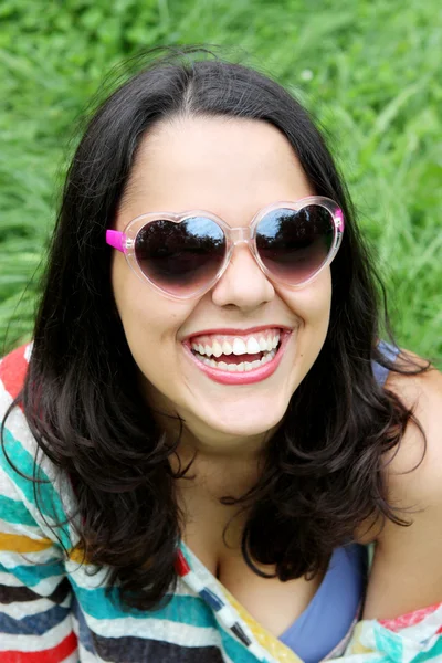 Beautiful young girl in sunglasses sitting on the grass — Stock Photo, Image