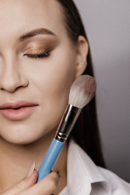 Makyajlı makyöz elinde fırça tutuyor.