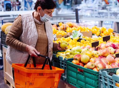 Tıbbi maskeli ve alışveriş sepetli büyükannem mağazadan ürünleri seçiyor. Salgın. Market alışverişi. Market..