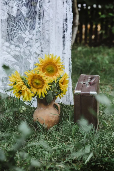 bouquet of sunflowers in an old jug near the old suitcase in the background curtains. Ukrainian product. Retro composition. Antique things in the garden. Selective focus. Under the open sky. Still