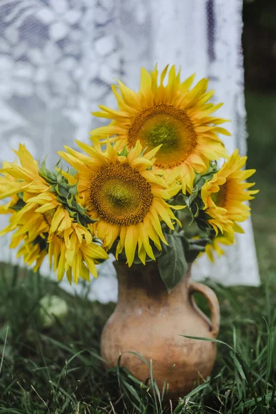 Bouquet of sunflowers close-up in an old jug in the background of curtains. Ukrainian product. Retro composition. Antiques in the garden. Selective focus. Open air. Still life. vertical photo