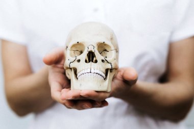 Kadınların elleri kafatasını tutar. Tıbbi elbise giymiş bir kadın. Bilim anatomisi. Cadılar bayramı