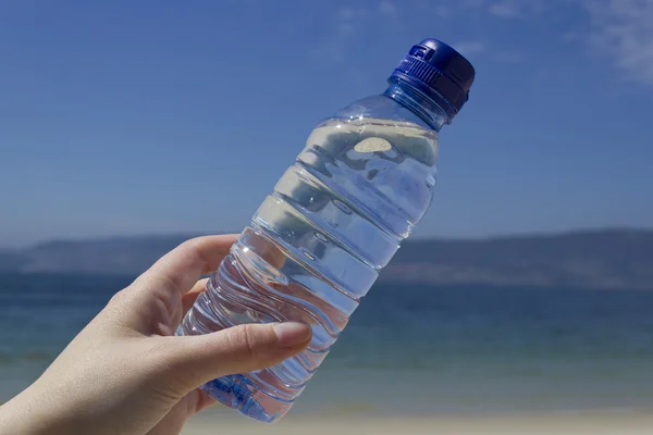 Mano di donna con una bottiglia d'acqua sulla spiaggia — Foto Stock