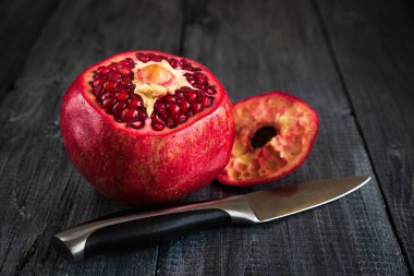 Koyu arkaplanda olgun nar ve üstü kesilmiş ahşap bir masa ve metal bir bıçak..