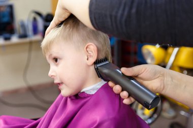 Küçük bir çocuk saçını kesmek için bir çocuk kuaföründe oturuyor..