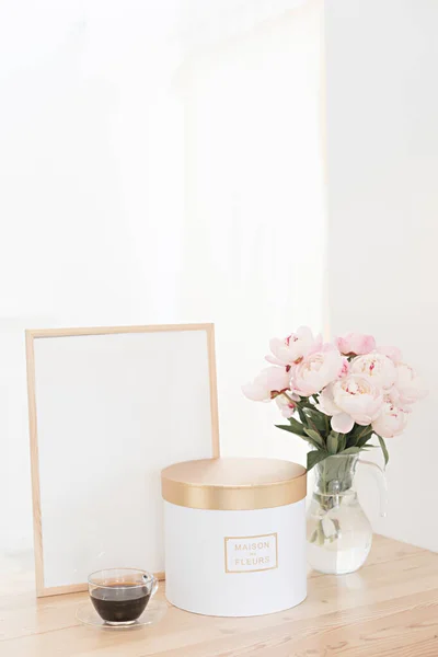 Κάθετη πλαίσιο και κουτί δώρου mockup σε ένα ξύλινο τραπέζι στην κουζίνα. Γυάλινη κανάτα με ένα μπουκέτο ροζ παιώνιες και ένα φλιτζάνι μαύρο καφέ. Σκανδιναβικό εσωτερικό στυλ. — Φωτογραφία Αρχείου