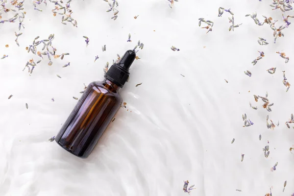 Amber bottle of lavender essential oil. Flat lay concept. Light background with water waves.
