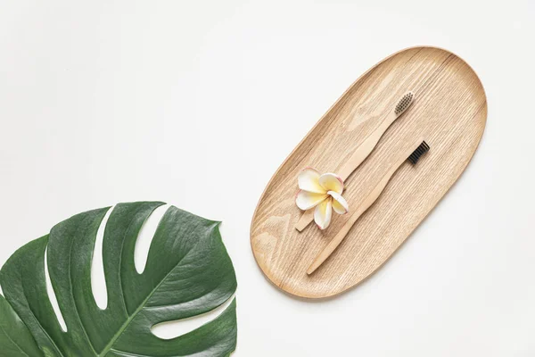 Bamboo toothbrush on a table with copy space on a white background. Styled composition of flat lay with tropical leaves and flowers. — Foto de Stock