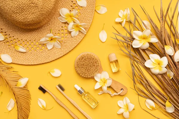 Bamboo toothbrush and dried palm leaf oil on a table with copy space on a yellow background. Styled composition of flat lay with tropical leaves and flowers. — Fotografia de Stock