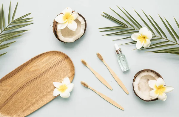 Bamboo toothbrush and bootle essential oil on a table with copy space on a white background. Styled composition of flat lay with coconut, tropical leaves and flowers. — Fotografia de Stock