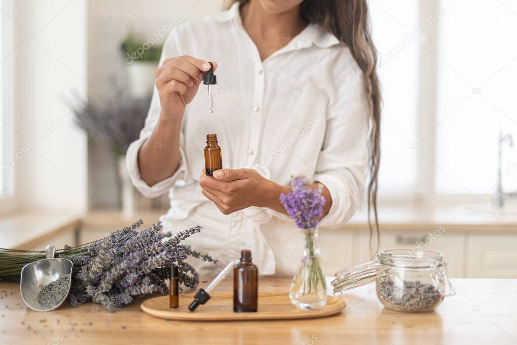 Essential oils of lavender in a glass dark bottle. The girl cares for the skin and hair. Scandinavian interior.