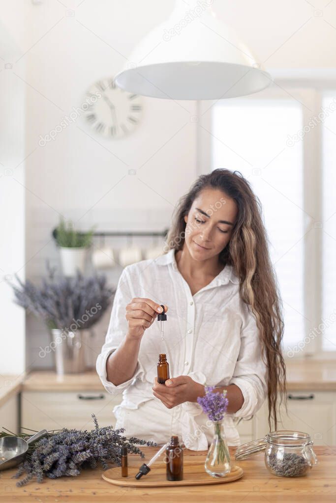 Essential oils of lavender in a glass dark bottle. The girl cares for the skin and hair. Scandinavian interior.