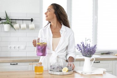Genç bir kız limon ve lavantadan limonata yapıyor. Yaz içkisi hazırlayan kadın
