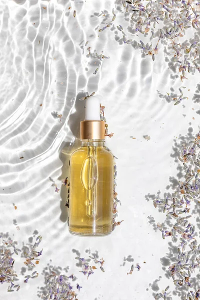 Amber bottle of lavender essential oil. Flat lay concept. Light background with water waves