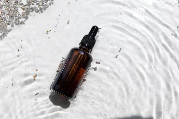 Amber bottle of lavender essential oil. Flat lay concept. Light background with water waves