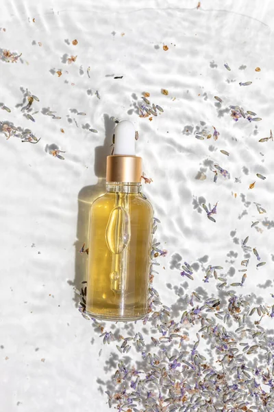 Amber bottle of lavender essential oil. Flat lay concept. Light background with water waves