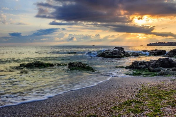 Ochtendzon stralen verlichten zanderige strand met kleine rotsen — Stockfoto