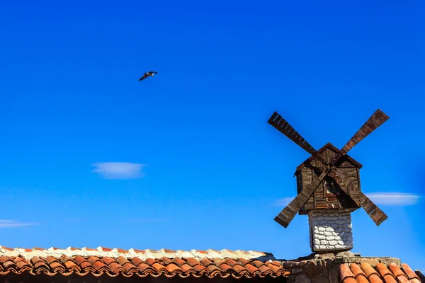 Windmill and seagul on background of blue sky over building — Stock Photo, Image