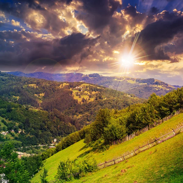 Villaggio su prato collinare con bosco in montagna al tramonto — Foto Stock
