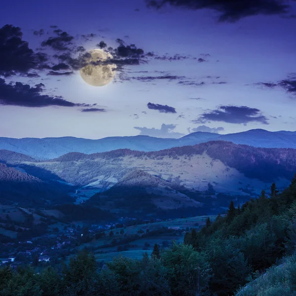 Villaggio sul prato collinare con foresta in montagna di notte — Foto Stock