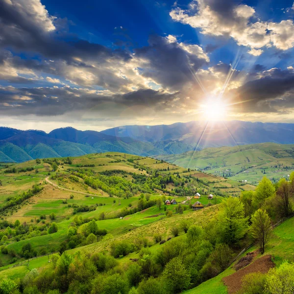 Aldeia no prado da encosta com floresta na montanha ao pôr do sol — Fotografia de Stock