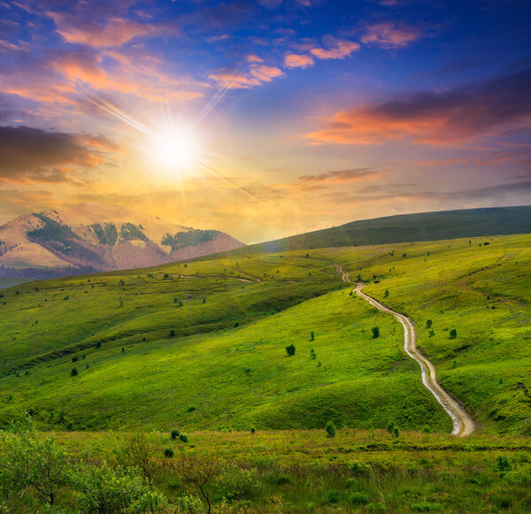 road through a meadow in high mountains at sunset