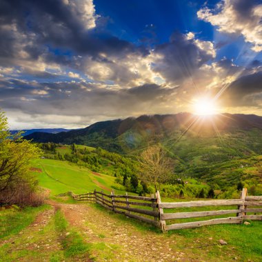 fence on hillside meadow in mountain at sunset clipart