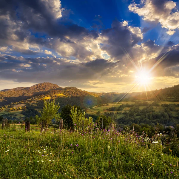 Aldeia no prado da encosta com floresta na montanha ao pôr do sol — Fotografia de Stock