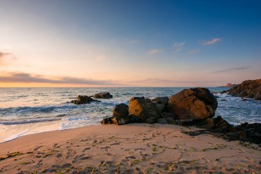 Güneşin doğuşunda kumlu sahilde kocaman taşlar. Sabah vakti Karadeniz 'de harika bir kadife sezonu tatili. Durgun dalgalar, İspanya kıyılarını yıkıyor. Ufkun üstündeki mavi gökyüzünde parlayan bulutlar