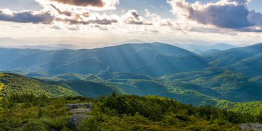 Dağlardaki açık hava macera manzarası. Güzel yeşil yaz manzarası. Akşam ışığında bulutlu bir gökyüzünün altındaki çimenli tepede taşlar. Açık hava doğa turizmi ve tatil konsepti