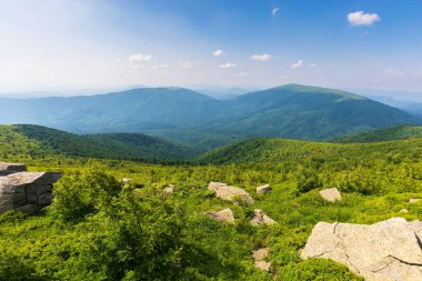 Yazın güzel dağ manzarası. Yüksek bir çayırdaki taşlar ve kayalar. Akşam ışığında yeşil çimenli tepe ile güzel bir arka plan. Manzaralı vadi manzarası. Bulutlu gökyüzü