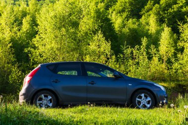 Turya, Ukrayna - 17 Mayıs 2021: doğa manzarasında küçük bir hatchback. Çayırdan geçen kırsal yolda bir araba. Tepedeki ağaçlar. Sabah güneşinde güzel bahar manzarası