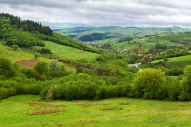 Dağlarda yağmurlu bir günde kırsal alan. Uzak vadideki köy. Baharda yeşil doğa manzarası. Gökyüzündeki bulutlar