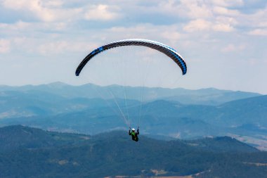 Dağ vadisinde yamaç paraşütü yapıyor. Açık hava sporları. macera ve seyahat konsepti. Yazın gökyüzünde bulutlar