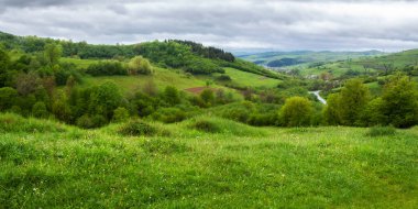 Dağlarda yağmurlu bir günde kırsal alan. Uzak vadideki köy. Baharda yeşil doğa manzarası. Gökyüzündeki bulutlar