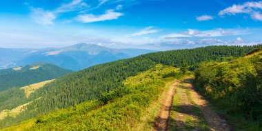 Yürüyüş yolu olan dağ manzarası. Yeşil orman tepeleri bir yaz sabahı. Yamaç boyunca bir patika manzarası. Mavi gökyüzünün altında, bulutlu bir tepe. geniş açı görünümü
