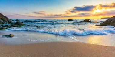 Gün doğumunda boş bir sahil. Denizin güzel manzarası. Dalgalar sahildeki kum ve taşları yıkıyor. Sabah ışığında parlayan bulutlar. sakin bir yaz tatili ve seyahat yeri konsepti