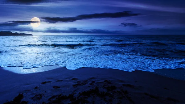 Geceleri kumsalda. Güzel bir deniz manzarası. Sakin dalgalar kıyıları yıkıyor. Dolunay ışığında parlayan bulutlar. Yaz tatili ve dinlenme konsepti
