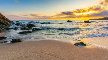 Gün doğumunda boş bir sahil. Denizin güzel manzarası. Dalgalar sahildeki kum ve taşları yıkıyor. Sabah ışığında parlayan bulutlar. sakin bir yaz tatili ve seyahat yeri konsepti