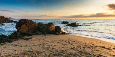 Sabah ışığında kumlu bir sahilde kayalar. Güneşin doğuşunda güzel bir deniz manzarası. Sakin dalgalar kıyıları yıkar. Rahatlama ve yaz tatili konsepti. ufukta muhteşem bulut manzarası