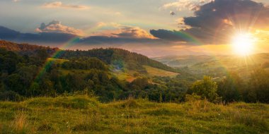 Gün batımında dağlık kırsal alan. Tepelerdeki ormanın yakınındaki kırsal alanlar ve otlaklar. Güzel sonbahar erken doğası manzarası Akşam ışığında gökyüzünde bulutlar