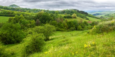 Dağlarda yağmurlu bir günde kırsal alan. Uzak vadideki köy. Baharda yeşil doğa manzarası. Gökyüzündeki bulutlar
