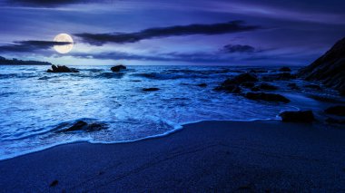 Geceleyin boş bir sahil. Denizin güzel manzarası. Dalgalar sahildeki kum ve taşları yıkıyor. Dolunay ışığında parlayan bulutlar. sakin bir yaz tatili ve seyahat yeri konsepti