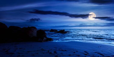 Geceleri kumlu sahilde kocaman taşlar. Dolunay ışığında Karadeniz 'de harika bir kadife mevsimi tatili. Sakin dalgalar kıyıları yıkıyor. Ufkun üzerindeki koyu mavi gökyüzünde bulutlar