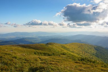 Karpatya dağlarında günbatımı manzarası. Akşam ışığında çimenli tepe. Pofuduk bulutlarla dolu muhteşem bir gökyüzünün altındaki uzak vadiye bak.