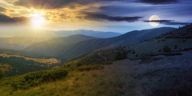 Yazın alacakaranlıkta Carpathian sıradağları. Gündüz ve gece zaman kavramını değiştirir. Orman tepeleri ve çimenli çayırları olan manzara güneşli ve aylı bir gökyüzünün altındaki vadiye doğru iniyor.