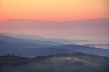 Gün doğumunda dağlık sisli bir manzara. Sonbahar kırsal bölgesi sisli manzarası. Güzel manzara sabah sisi ile dolu uzak vadiye.