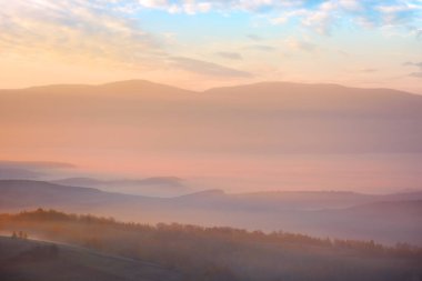 Sisli bir sonbahar sabahı. Gün doğumunda dağlarda güzel bir manzara. Orman tepeleri ve uzak vadide parlayan sis